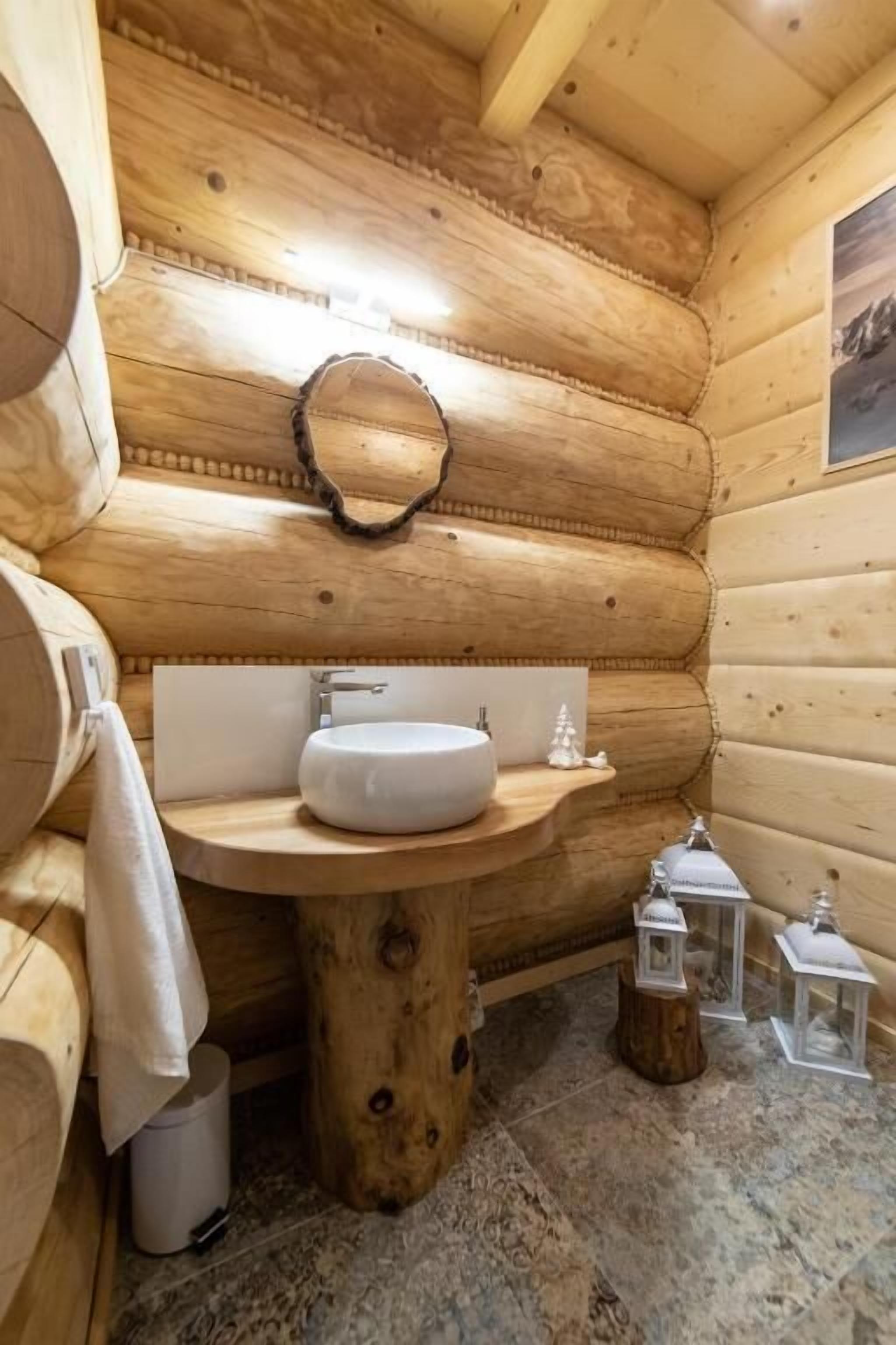 Un baño de cabaña de madera con un lavabo redondo, paredes de madera y un espejo.