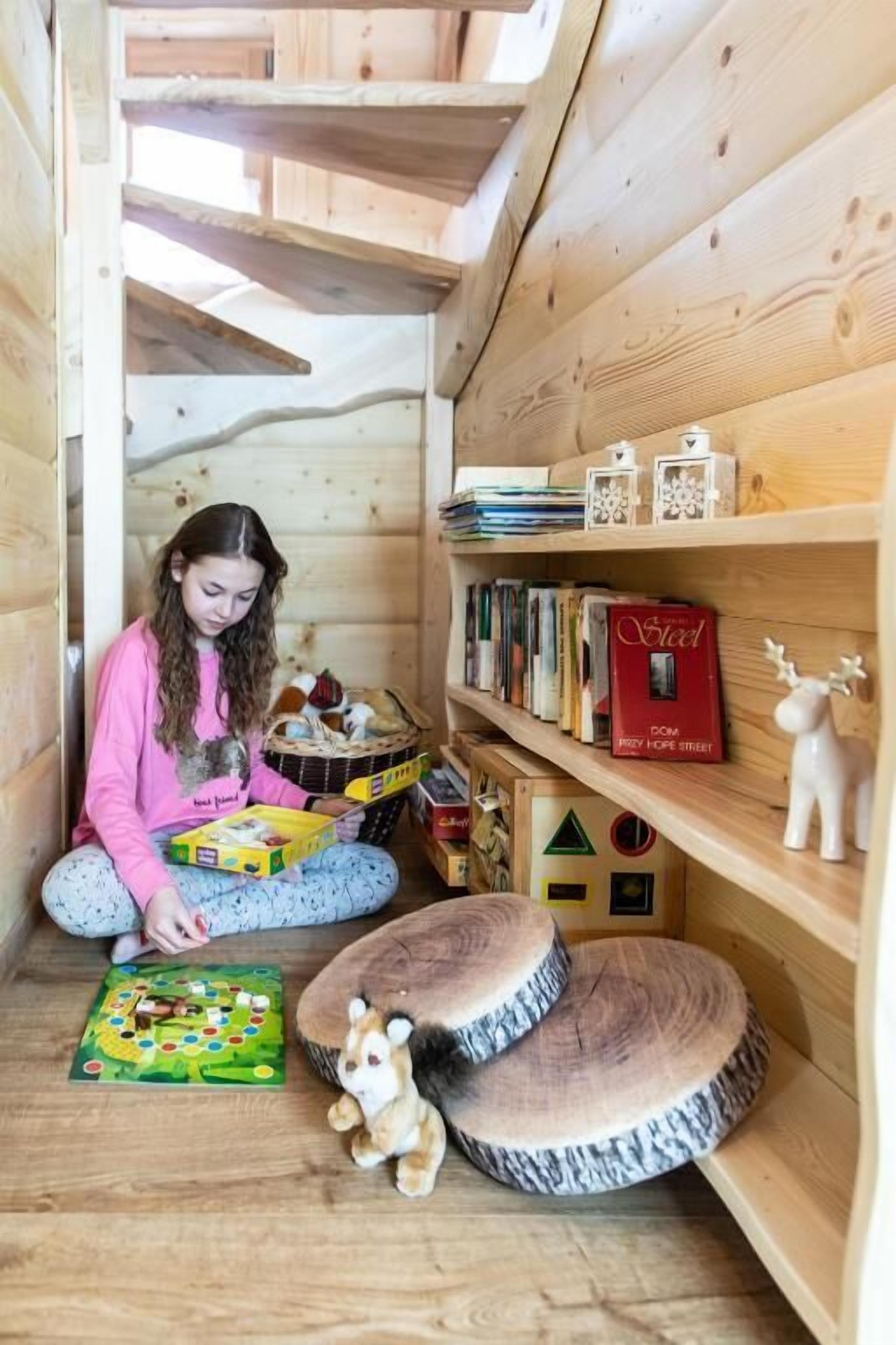 Une pièce en bois avec un plafond en pente, une bibliothèque remplie de livres et d’objets décoratifs, et un enfant qui joue à un jeu de société.