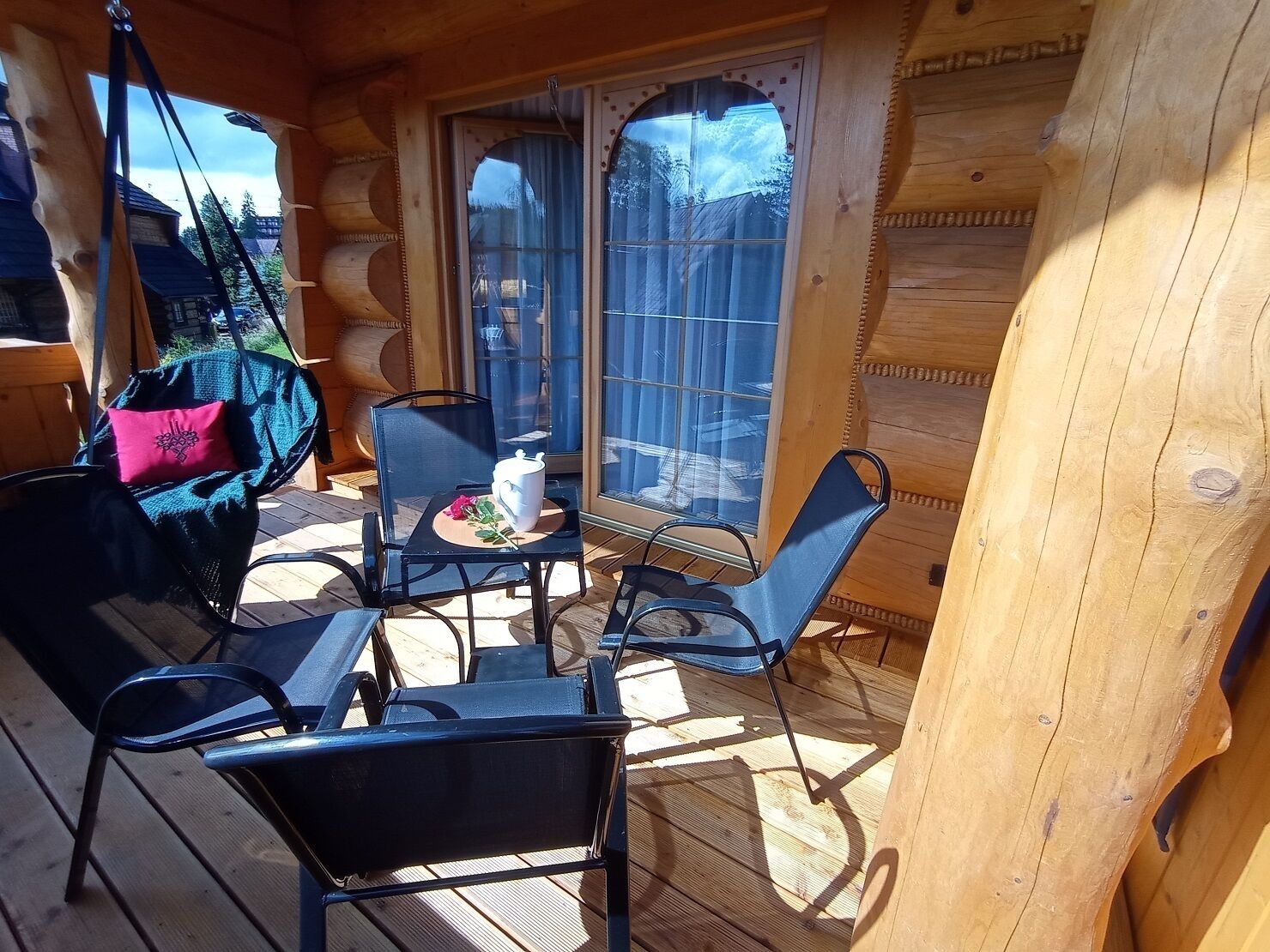 A wooden cabin with a deck, a hanging chair, and a table with chairs.