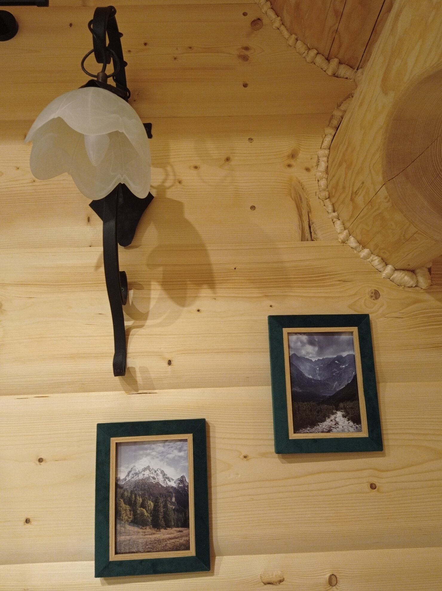 Un mur en bois orné de deux photographies encadrées et d’un luminaire suspendu.