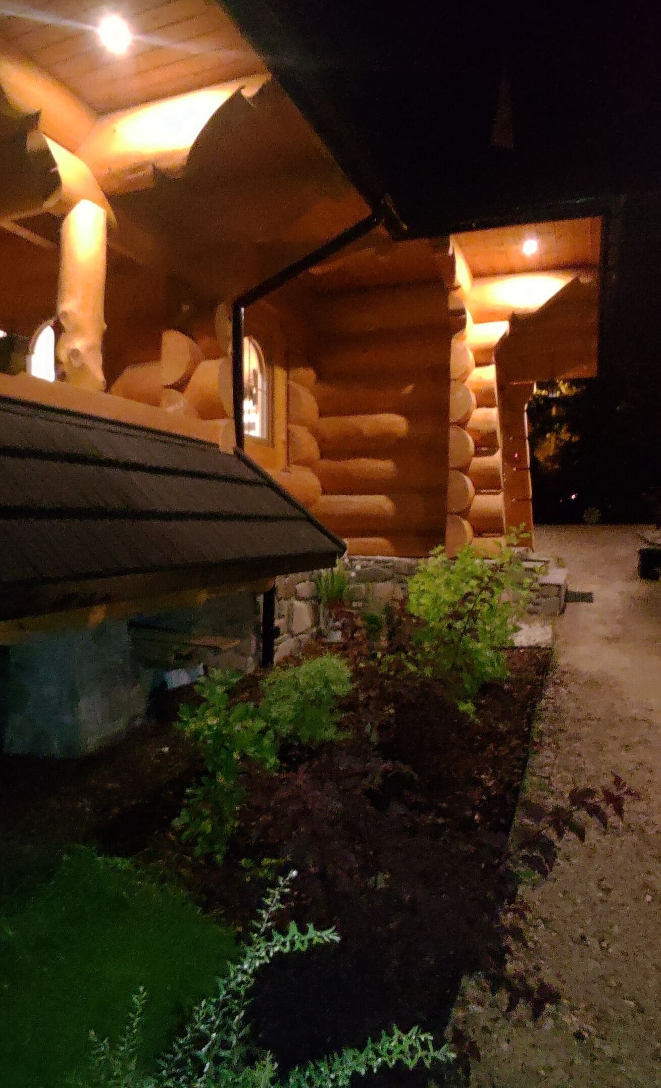 A log cabin with a stone foundation, a covered porch, and a well-maintained garden area.