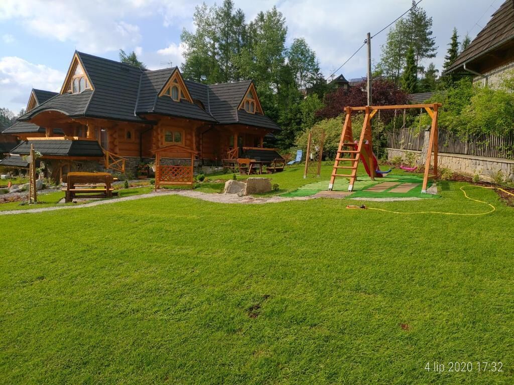 A wooden cabin with a sloped roof, a wooden swing set, and a well-maintained lawn.