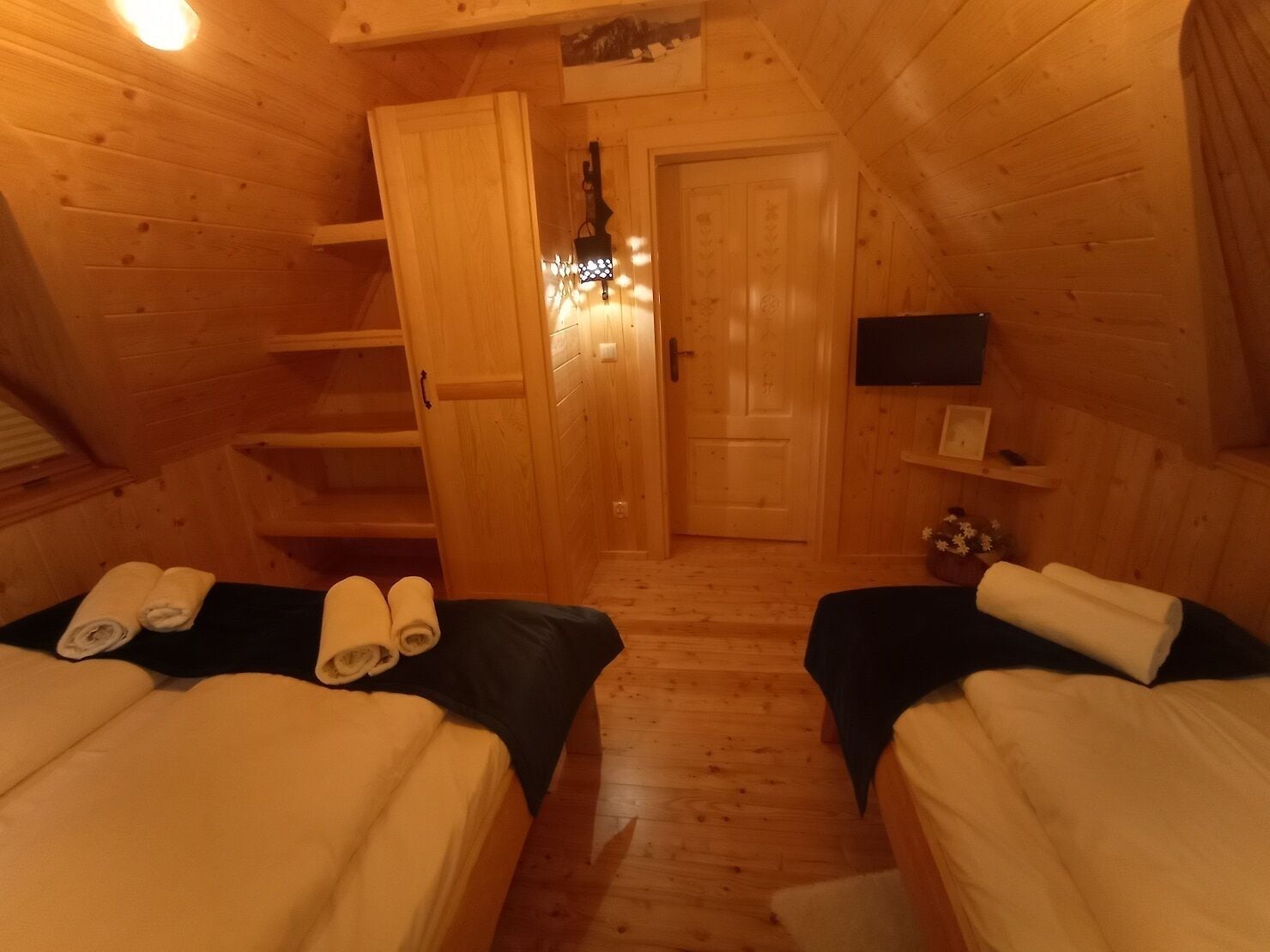 A cozy wooden cabin room with two beds, a small TV, and a door leading to another room.