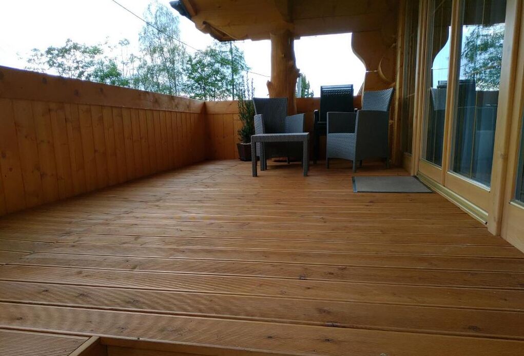 Une terrasse en bois dotée d’un espace salon couvert, d’une plante en pot et d’une porte-fenêtre coulissante.