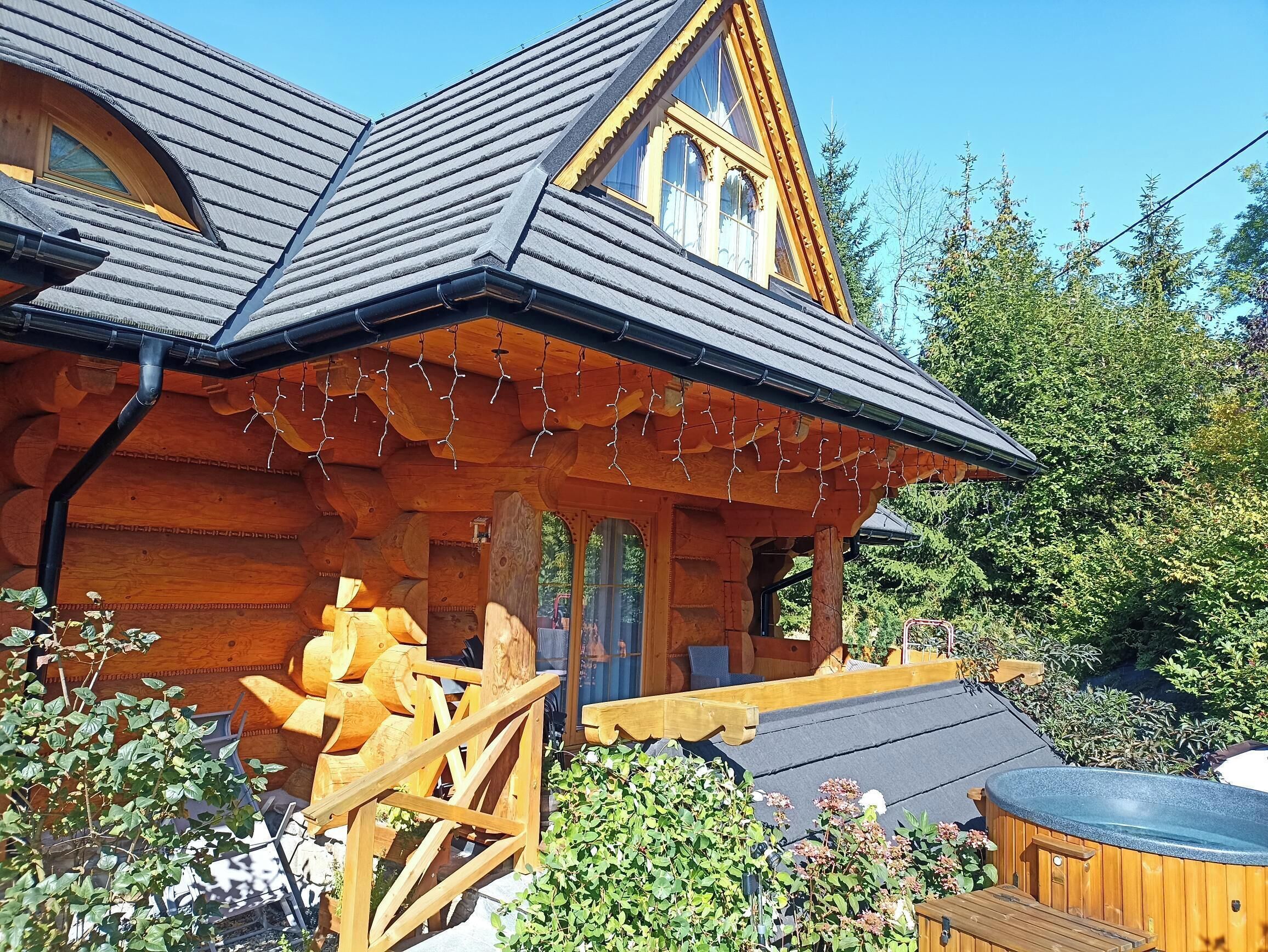 A log cabin with a sloped roof, wooden exterior, and a hot tub in the foreground.