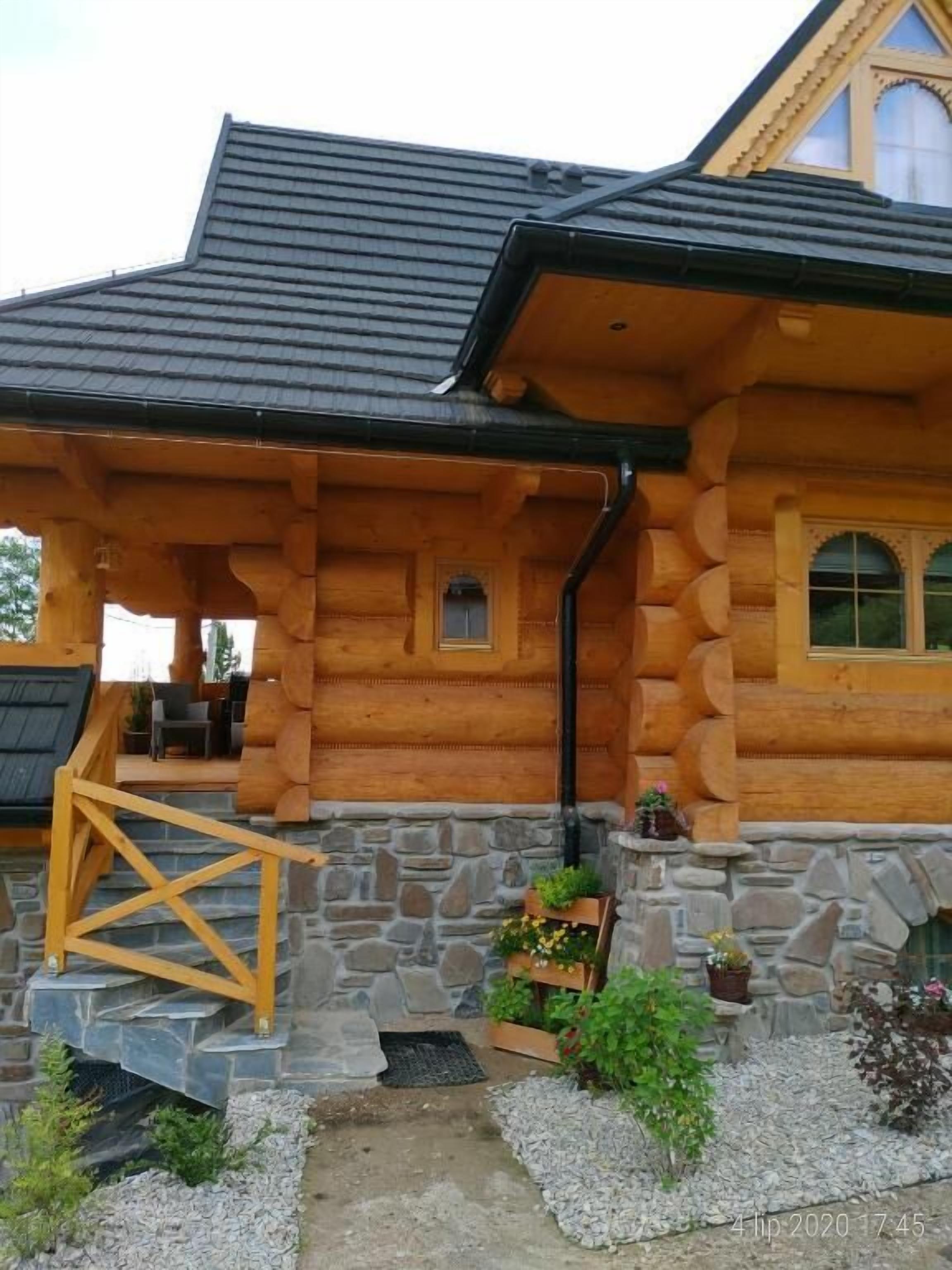 A log cabin with a stone foundation, wooden porch, and a small garden area with potted plants.