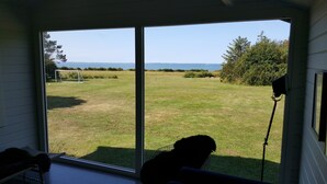 A room with a large sliding glass door leading to a grassy yard with a soccer goal, trees, and a clear view of the ocean. - Panoramic seaview from small island (Omø)