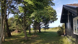 A house with a black exterior, a visible window, and a grassy yard with trees. - Panoramic seaview from small island (Omø)