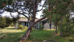 A house with a large tree in the foreground, a swing set, and a grassy yard. - Panoramic seaview from small island (Omø)