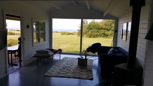 A cozy room with a large sliding glass door leading to a grassy outdoor area. Inside, there is a sofa, a small table, and a rug. - Panoramic seaview from small island (Omø)