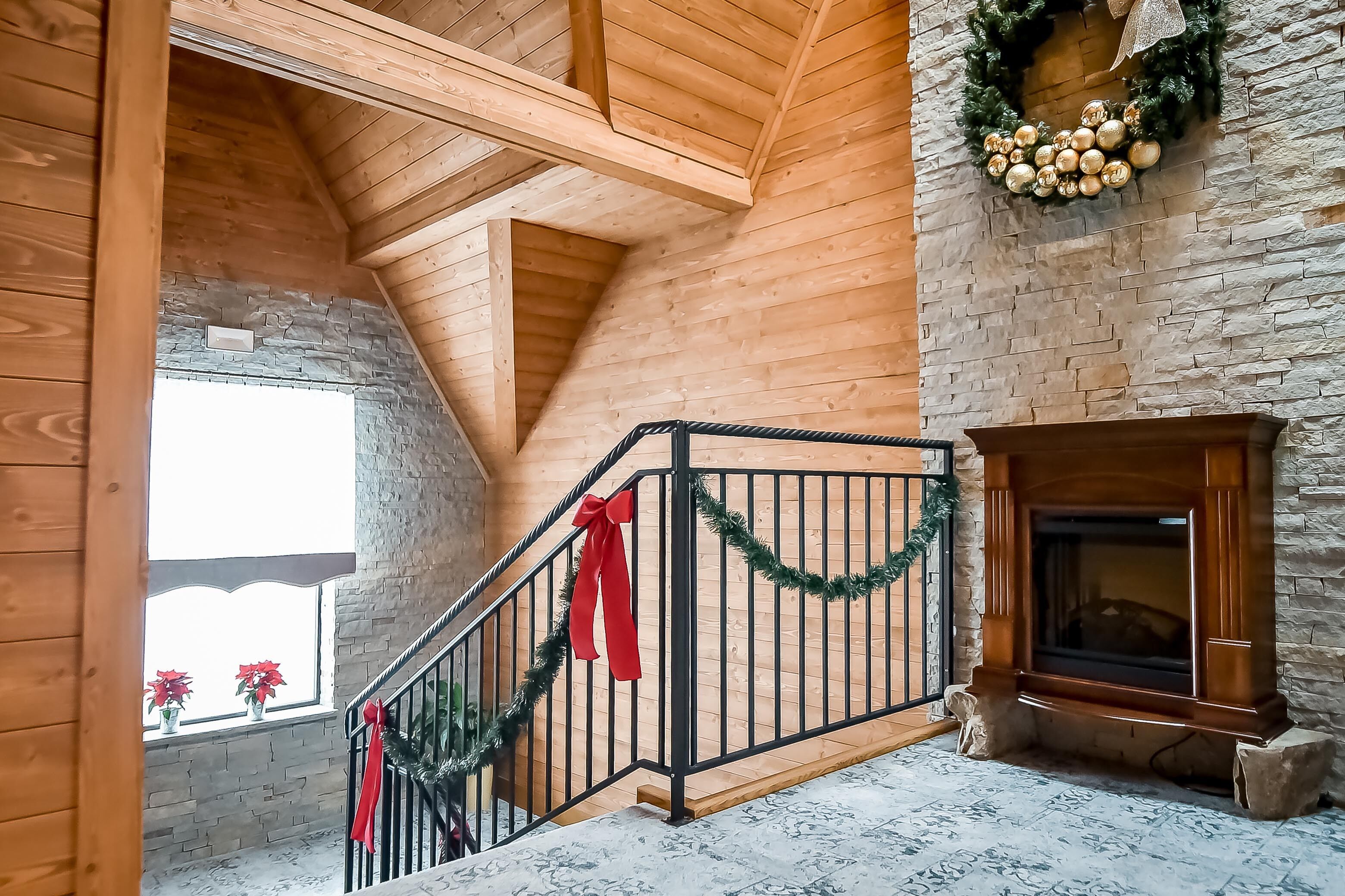 A wooden interior with a fireplace, a staircase with red and green decorations, and a stone wall.