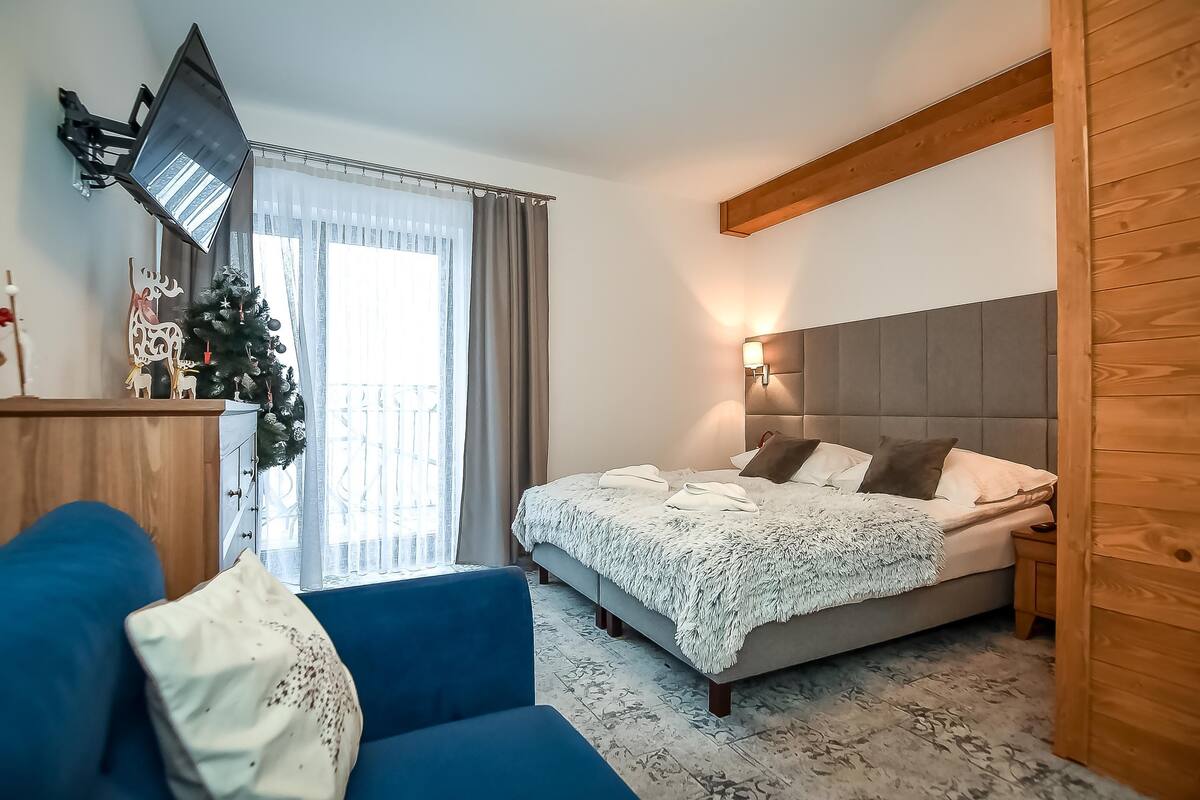 Un dormitorio con una cama, un sofá azul, una mesita de noche, un televisor montado en la pared y un árbol de Navidad.