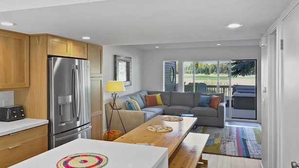 A modern kitchen with a built-in refrigerator, wooden cabinets, and a white countertop. There is a dining area with a bench and a table, and a sofa in the background. - Open Floor 71 Vantage Family Condo by RedAwning (Park City)