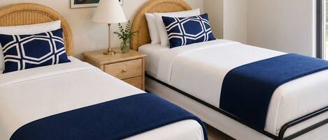 A hotel room with two beds, a nightstand, a lamp, a painting, and a window.
