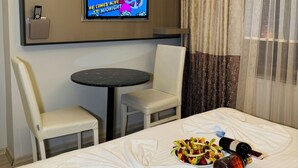 Quarto de hotel com uma cama, televisão fixada na parede, uma mesinha com cadeiras e uma janela com cortinas.