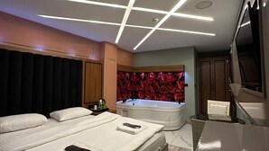 Quarto de hotel moderno com uma cama grande, área de estar separada e uma banheira.