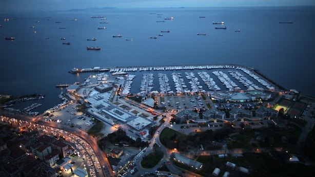 Vista aérea de um porto com muitos barcos atracados, um amplo estacionamento e edifícios ao redor.