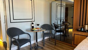 Quarto de hotel com área de jantar, com duas cadeiras, uma pequena mesa, uma garrafa de vinho e um copo, e um prato de comida.