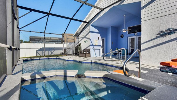 Ein Schwimmbad mit Glasüberdachung, Deckenventilator und einer kleinen Sitzecke mit Handtüchern.