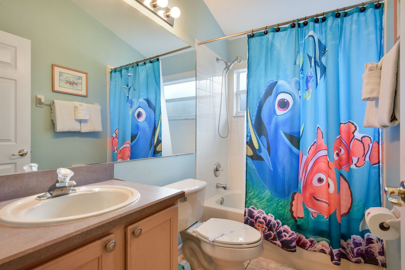 Un baño con lavabo, inodoro, ducha y cortina de ducha con personajes animados.