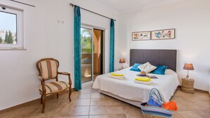 Ein Schlafzimmer mit einem Bett, einem Sessel, einem Koffer und einem Fenster.