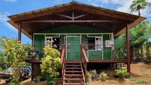 Un petit bâtiment d’un seul étage, à l’extérieur vert, avec un escalier en bois menant à un porche.