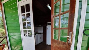 Un bâtiment en bois peint en vert, avec une porte en bois donnant sur un espace cuisine.