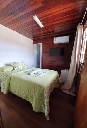 Une chambre avec un plafond en bois, un lit avec une literie à motifs floraux, une télévision et un appareil de climatisation.