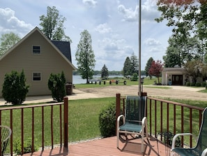 A deck with a rocking chair, a small table, and a view of a lake and a house.