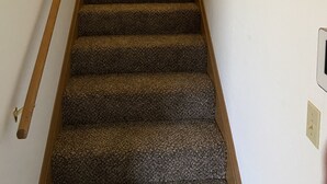 A carpeted staircase with a wooden handrail and a wall-mounted clock. - Basics 90's Condo 906 Downtown Moses Lake (Moses Lake)