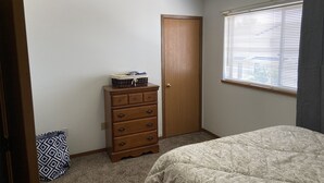 A bedroom with a bed, a dresser, a window with blinds, and a door. - Basics 90's Condo 906 Downtown Moses Lake (Moses Lake)