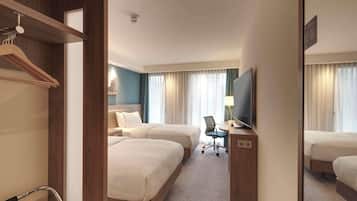 Quarto de hotel com duas camas, uma escrivaninha com cadeira, televisão e espelho.