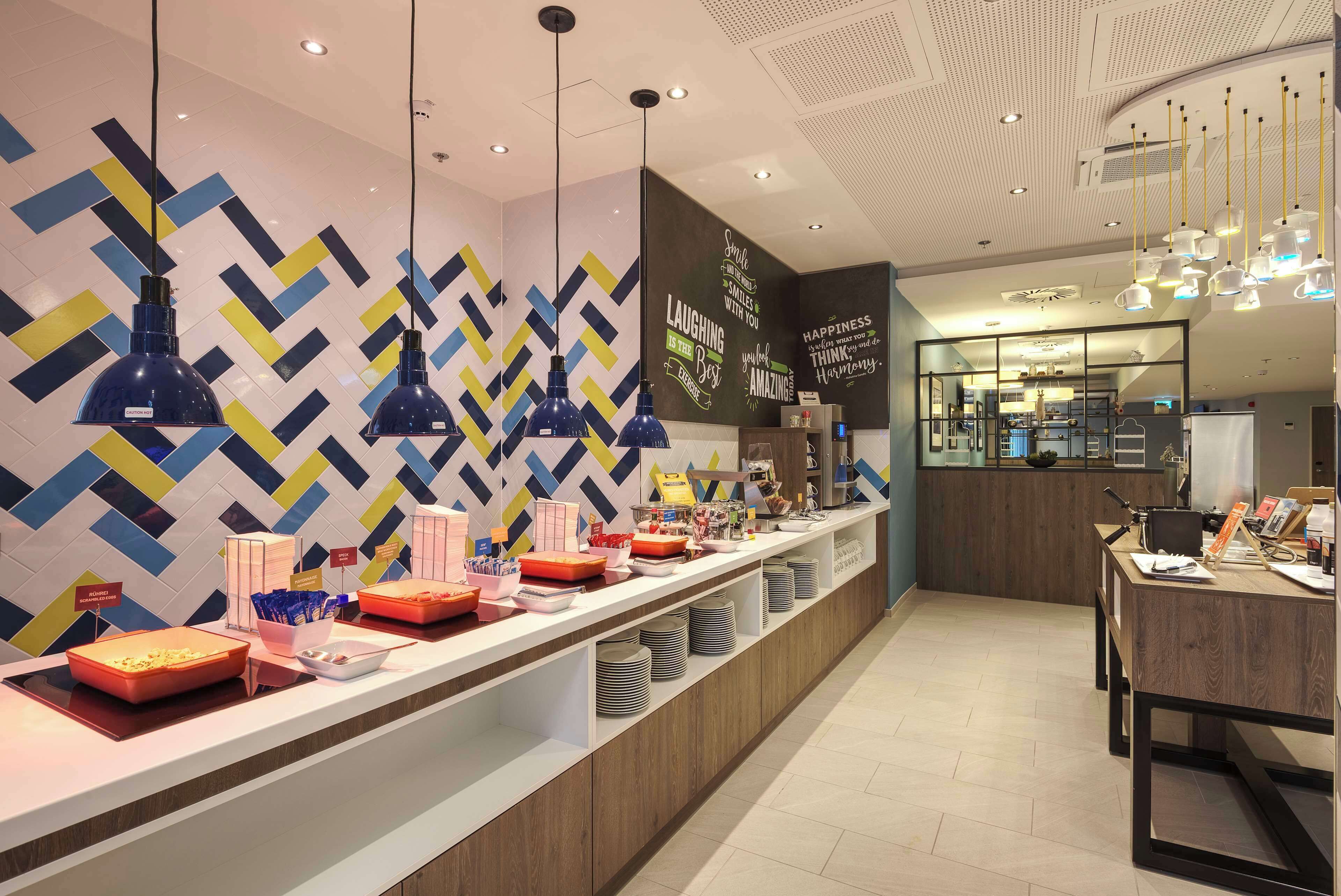 Een moderne hotelontvangst met een lange balie, blauwe hanglampen en een geometrisch patroon op de muur.