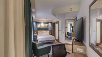 Une chambre d’hôtel comprenant un lit, un bureau avec une télévision, une chaise et un miroir.