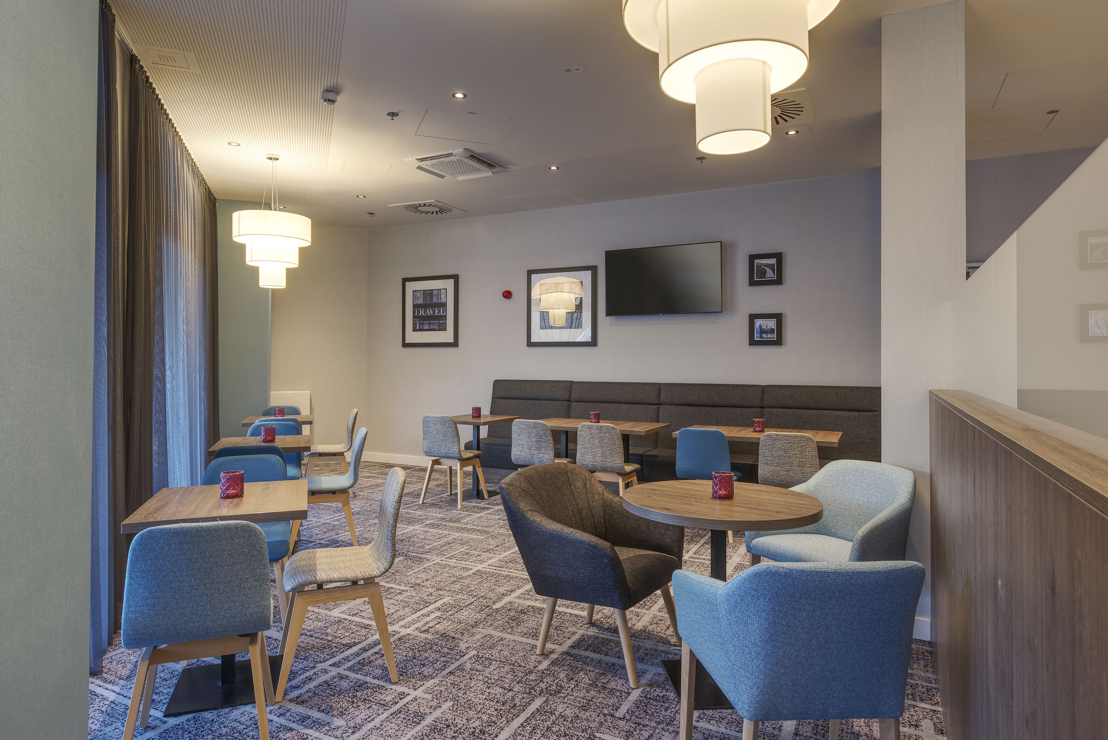 Een hotel lobby met zithoeken, een aan de muur bevestigde televisie en een kamerbreed tapijt met een patroon.