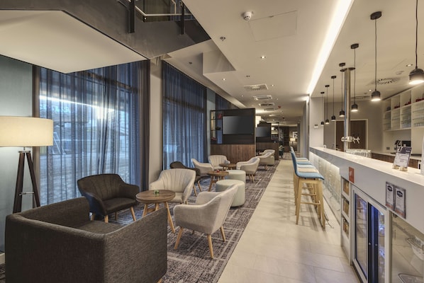 A modern hotel lobby with seating areas, a reception desk, and a bar. - Hampton by Hilton Stuttgart City Centre (Stuttgart)