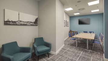 A conference room with a large table, blue chairs, a flat-screen TV, and a cityscape painting on the wall.