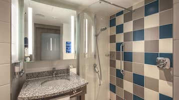 A modern bathroom with a granite countertop sink, a glass-enclosed shower, and a tiled wall with a blue and beige pattern.
