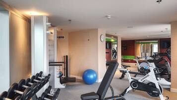 Un gimnasio con equipo de ejercicio, una pelota de pilates azul y una bicicleta de spinning.