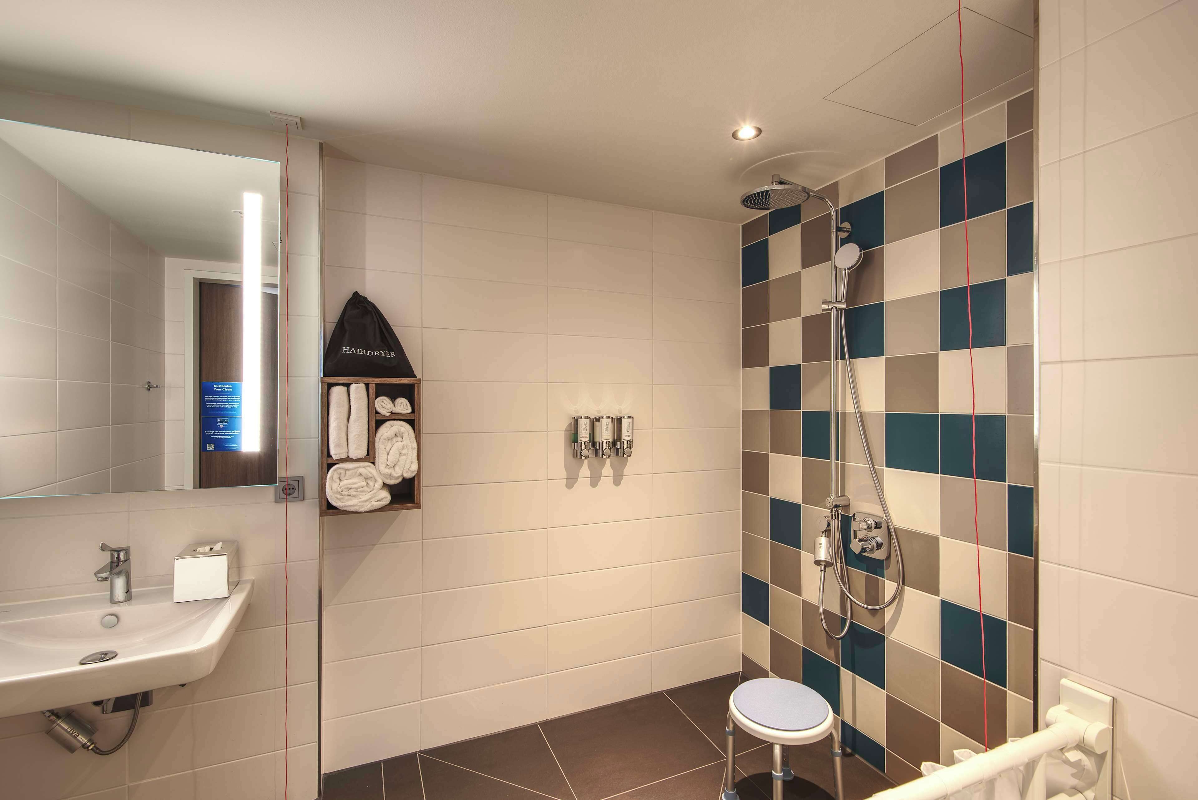 A bathroom with a sink, mirror, towel rack, and shower with a checkered tile wall.