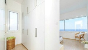 Ein modernes, minimalistisches Zimmer mit großem Kleiderschrank, einem Korbwäscheschale, einem Korbstuhl und Meerblick durch große Fenster.