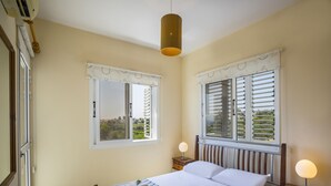 Ein Schlafzimmer mit einem Bett, zwei Nachttischen, einem Fenster mit Fensterläden und einer Klimaanlage.