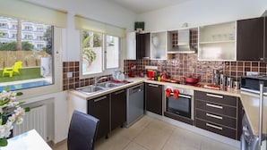 Een moderne keuken met een vaatwasser, oven en magnetron. Er is een raam met uitzicht op een zwembad en een stoel buiten.