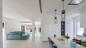 A modern kitchen with a central island, a dining area with a sofa, and a view of a pool and outdoor area. - Imagine Your Family Renting This Luxury Contemporary Style Villa in Protaras, Protaras Villa 1487 (Paralimni)