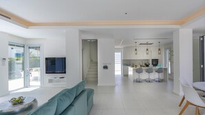 A modern living room with a sofa, a TV, and a kitchen area with bar stools. - Imagine Your Family Renting This Luxury Contemporary Style Villa in Protaras, Protaras Villa 1487 (Paralimni)