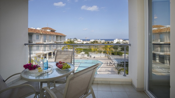 Ein Balkon mit Tisch für zwei Personen, einem Pool und Blick auf das Meer und die Gebäude.