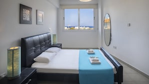 Ein Schlafzimmer mit Bett, Nachttisch, Lampe, Fenster mit Blick und einem Spiegel an der Wand.