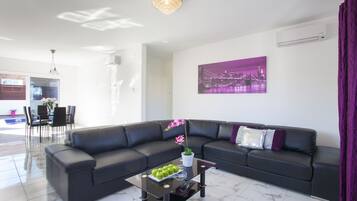 A modern living room with a black leather sofa, a glass coffee table with green apples, and a purple cityscape painting on the wall.