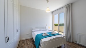 Ein Schlafzimmer mit Bett, Fenster mit Vorhängen, Heizkörper und Kleiderschrank.