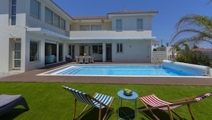 Ein modernes, zweistöckiges Haus mit Swimmingpool, Sitzgelegenheiten im Freien und einem gepflegten Rasen.